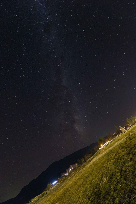 The Milky Way arching over Lake Tekapo, with the lights of the township strung along the dark hillside below