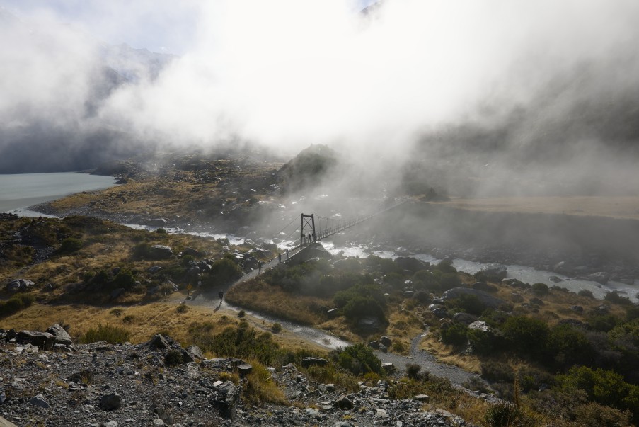 A swing bridge on the Hooker Valley Track as low cloud rolls down the valley and swallows the mountains behind it