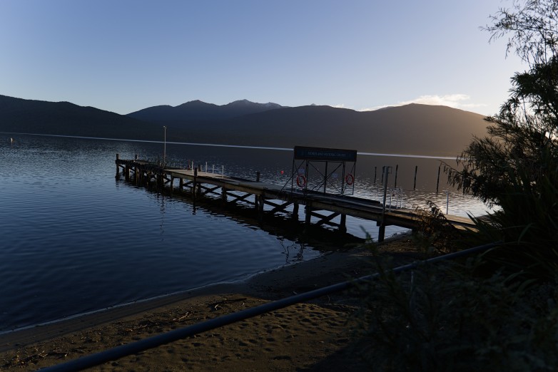 A wooden jetty reaching out into Lake Te Anau at dusk, the Fiordland ranges silhouetted beyond