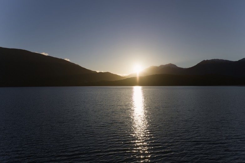 The sun setting behind the mountains across Lake Te Anau, laying a bright path of light over the water