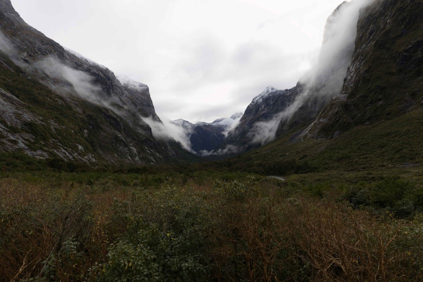 Low cloud pouring over the snow-dusted walls of a steep valley on the road to Milford Sound